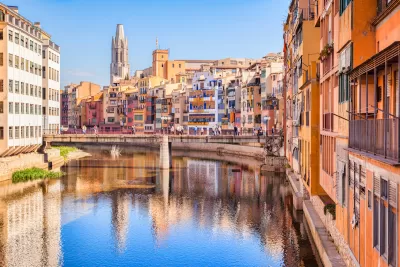 Old residential buildings along canal with ornate church in background in Girona, Catalonia, Spain.