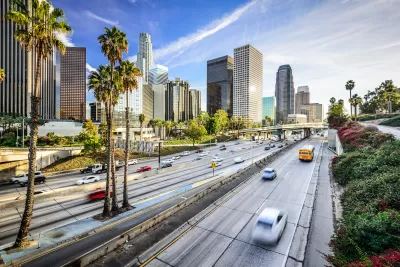 View of traffic on freeway with Los Angeles skyline and palm trees in background
