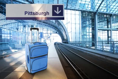 Blue suitcase sits on empty train platform with sign above labeled "Pittsburgh."