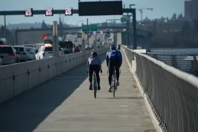Two cyclists riding on a protected bike lane on a bridge in Seattle with traffic on their left.