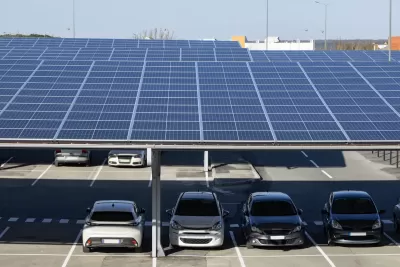 Solar panels installed as shade panels over parking lot with small cars parked underneath.