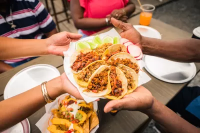 Close-up of multiple hands holding up plate of street-style tacos arranged in circular shape.