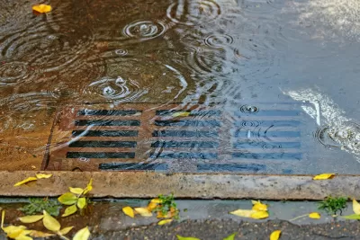 A leaf-free rusty street drain covered in a few inches of water.