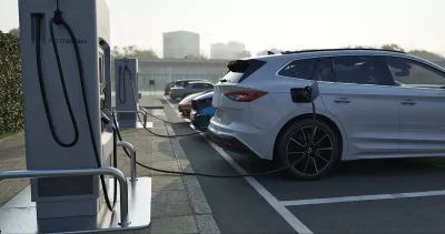 Row of vehicles parked and plugged in at EV charging station.