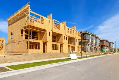 Wood-frame multifamily housing units under construction on a street in low-density area or suburb.