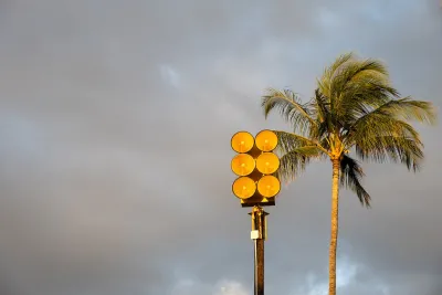 Tsunami sirens installed on top of pole in front of tall palm tree in golden stormy sky in Maui, Hawaii.