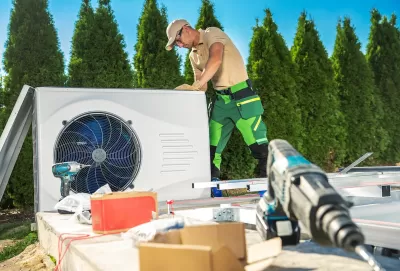 HVAC technician on roof installing heat pump with tools in foreground.