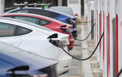 Close-up of four Tesla sedans parked and plugged in at charging station.