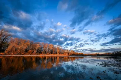 View of calm Maumee River with fall foliage on other side at sunset.