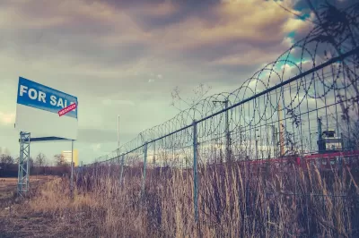 Fence with barbed wire and For Sale sign around vacant field.