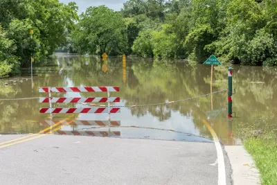 Flooded road with red and white gate barrier blocking entry in Houston, Texas.