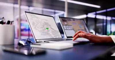 Close-up of laptop with GIS parcel map open and hand resting on keyboard in modern office.