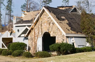Front view of stone home with severe tornado damage and portions of roof ripped off.