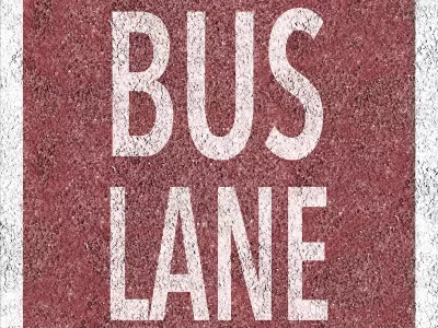 Overhead view of white BUS LANE sign painted on red background on concrete street.