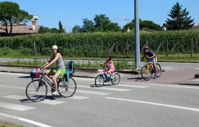 Woman and two children riding bikes across a striped crosswalk.