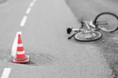 Blurred black and white image of bicycle laying down in road with orange traffic cone in foreground.