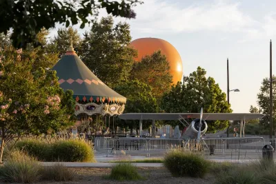 Afternoon light illuminates the landscape with orange tethered hot air balloon, vintage airplane, and carousel at Great Park in Irvine, California.