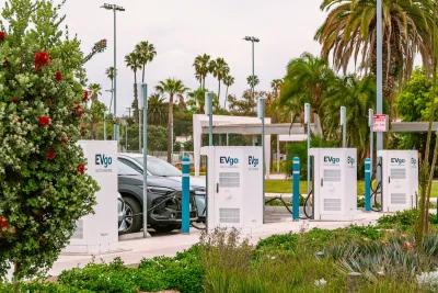 Cars parked and plugged in at an EV charging lot in Santa Monica, California surrounded by palm trees.