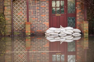 Sandbags stacked in front of a red door on a brick building with ground in front flooded with water