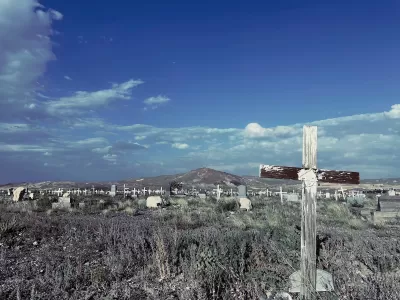 Old cemetery with weathered wooden cross grave markers in Goldfield, Nevada with mountain in background and blue sky.