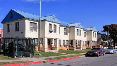A row of tan homes with blue roofs along a road.