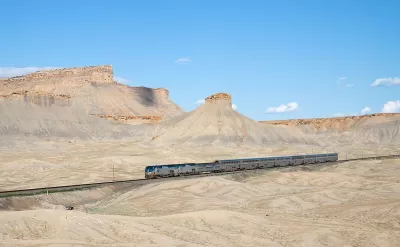 An Amtrak train passing through desert landscape with mesas in Utah.