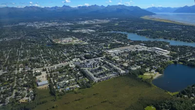 An aerial view of the Anchorage metropolitan area shows sprawling development surrounded by tall mountains.
