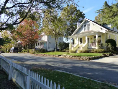 Large historic homes and white picket fences line a street.