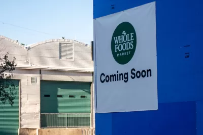 Austin, TA sign reading "Whole Foods Coming Soon" adorns a blue wall across the street from warehouses.