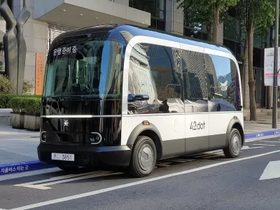 A small boxy driverless shuttle pulled up to a curb.