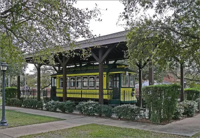 Yellow vintage Houston streetcar labeled Bellaire parked on display under covered carport surrounded by wrought iron fence in Houston, Texas.