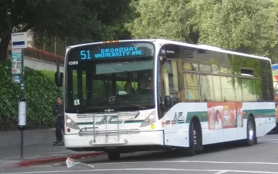 White bus pulling up to sidewalk bus station in Berkeley, California.
