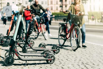 Parked electric scooters on a sidewalk with person walking bike in the background