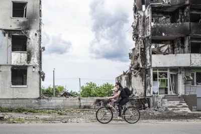 Woman and child ride bike past war-destroyed buildings in Borodyanka, Ukraine.