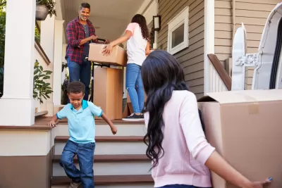 A family of Black Americans brings moving boxes into a home.
