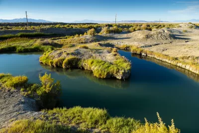 A hot springs in a low-lying desert area, with mountains in the distant background.