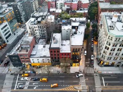 A block of the Bowery in New York City seen from high above, with taxis and other cars passing on the street in front of the buildings.
