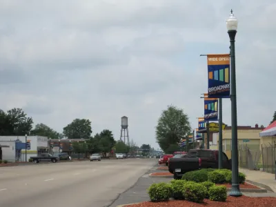 Wide, empty street with decorative town banners on light posts and water tower in background in West Memphis, Arkansas.
