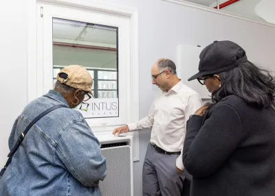Two Black women and a white man look at a window equipped heat pump in the showroom apartment.