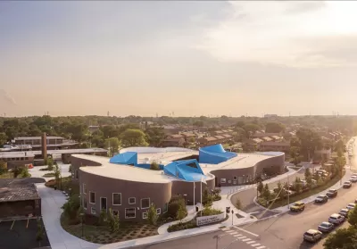 A large, multi-use building is adorned with blue canopies, pictured in the sunset of an urban landscape.