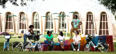 Promotional photo of diverse group of young people sitting on colorful bench with their Bublr bike share e-bikes parked in front of them.