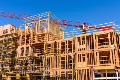 Wood-framed apartment building under construction with red crane in background