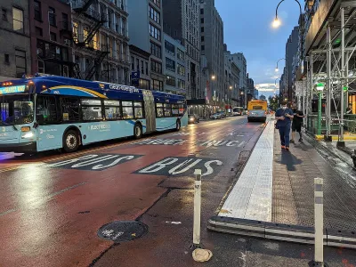 Blue and turquoise New York City bus at night on a red painted bus lane.
