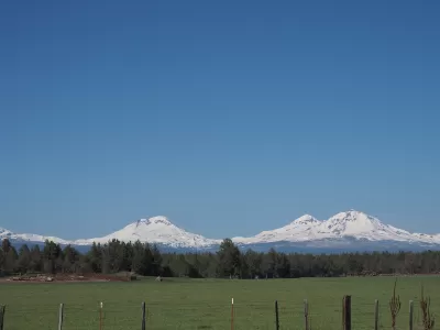 The Three Sisters, snow-covered mountains in Central Oregon, are visible in the distance beyond a farm.