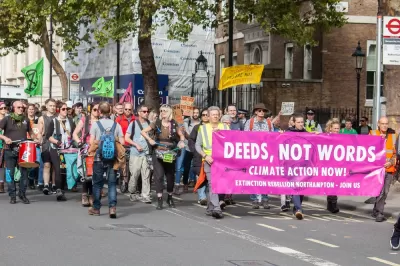 A group of protests with signs and drums walk down the street.