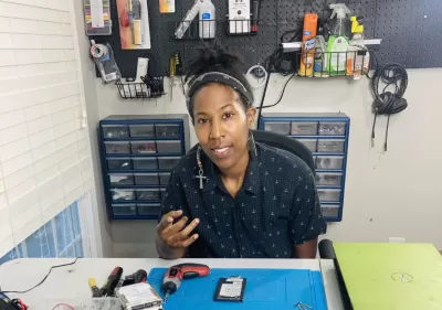 A Black woman works in a shop to prepare electronics for recycling..