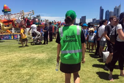 A person in a bright green vest with the words "Covid Marshall" patrols a street fair in Australia.