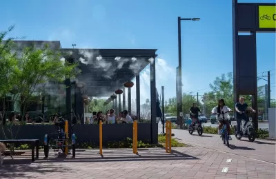 People ride bikes past outdoor restaurant patio with misters in Culdesac car-free development, Tempe, Arizona.