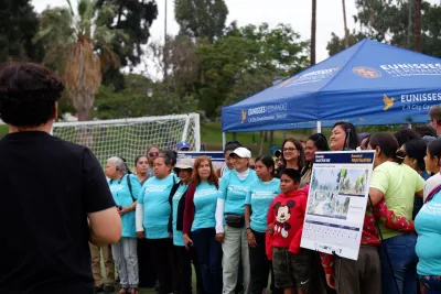 Crowd at event unveiling MacArthur Park transformation project standing next to display board with renderings.