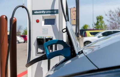 An electric vehicle is plugged into a charging station. A sticker reads “charge America” on the station.